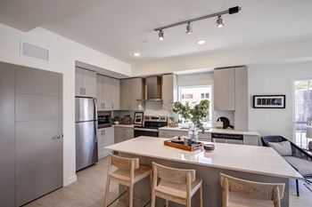 A modern kitchen with a white island and wooden chairs.